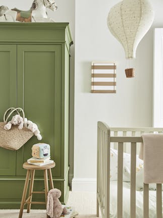 Calm nursery space with a green (Green Stone - Pale) wardrobe on the left and a crib on the right with a side table and fluffy toys on the floor.