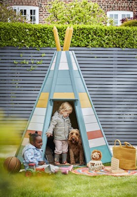 Multi colored tee-pee in a back yard in front of a paneled fence in dark blue (Juniper Ash) with two children and a dog playing.