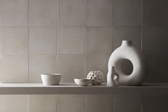 Close-up of a wall comprised of light grey square tiles painted in 'French Grey' with shelves holding light grey ornaments.