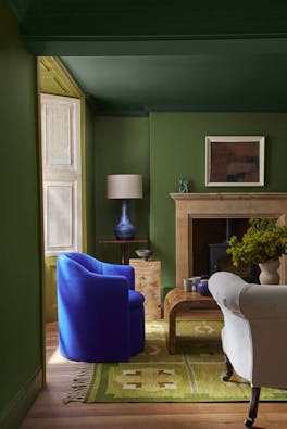 Living room painted in deep green 'Hopper' with a dark green ceiling above a fireplace and a bright blue armchair.