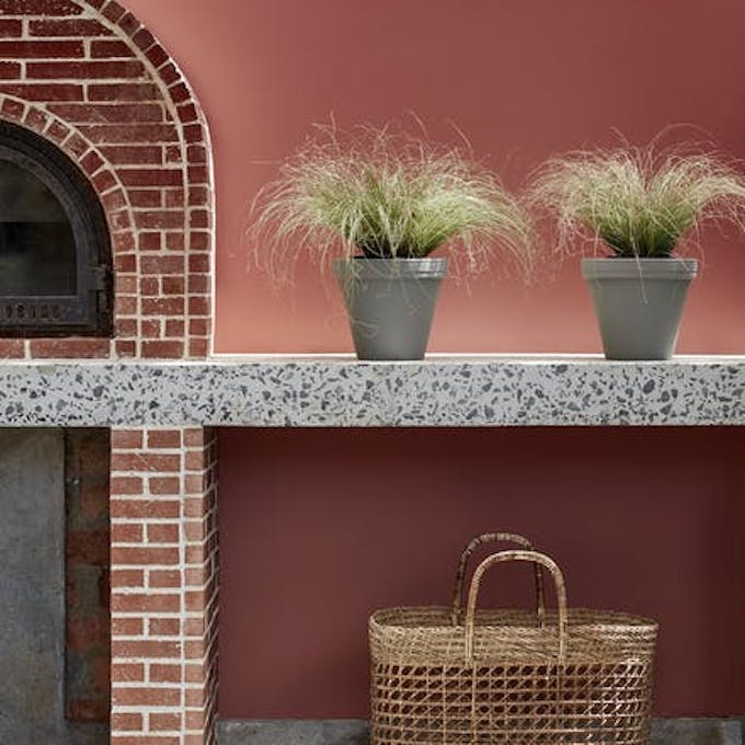 Outdoor kitchen painted in deep terracotta red 'Tuscan Red' with brickwork, plants and a basket.