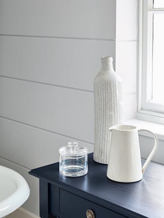 Close-up of a wall painted in light grey (Gauze) and a contrasting blue-black side table in Basalt with ornaments on top.