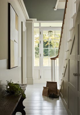 Hallway painted in four graduating shades of neutral 'Portland Stone' with a white wooden floor and a staircase to the right, looking out to a garden.