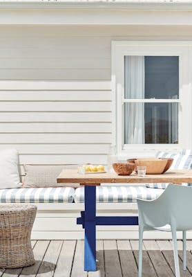 Outdoor dining area with off white paneled wall (Linen Wash) with a striped cushioned chair and wooden table.