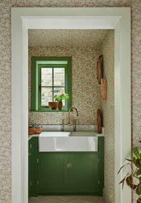 Pantry featuring two colourways of the floral wallpaper 'Spring Flowers' with dark green woodwork and a window above a sink.