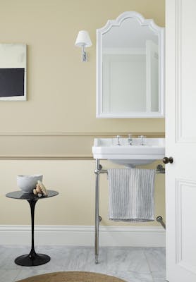 Bathroom painted in a different shades of warm neutral 'Travertine' with a free standing sink, white mirror and small table.