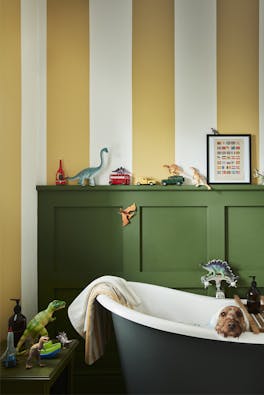 Yellow (Yellow-Pink) and white (Silent White) striped bathroom walls with deep green (Hopper) panelling and bathtub with a dog sat inside.