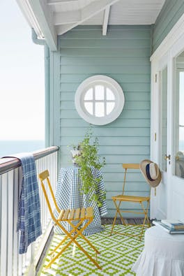 Sea front balcony painted in Celestial Blue with yellow (Bassoon) chairs, a round window and a green patterned floor.