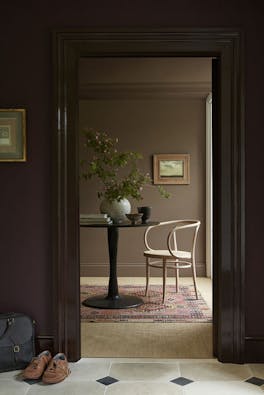 Hallway painted in aubergine shade 'Cordoba' looking into a study painted in mid-brown shade 'Scullery' with a chair and table.