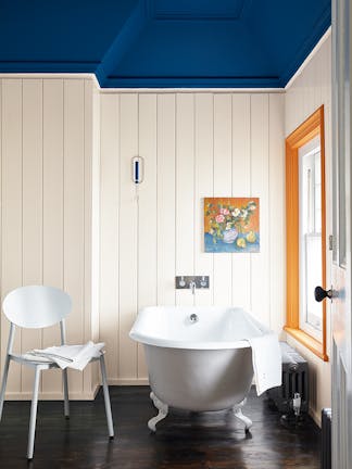 Bathroom with paneled walls painted in warm white shade 'Flint' and the ceiling painted in 'Deep Space Blue' with a bathtub and chair.