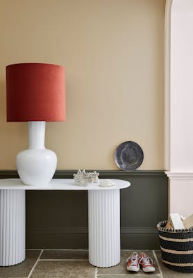 Pale brown neutral hallway (Lute) with lower wall painted in grey green (Pompeian Ash) and a white side table and large lamp.