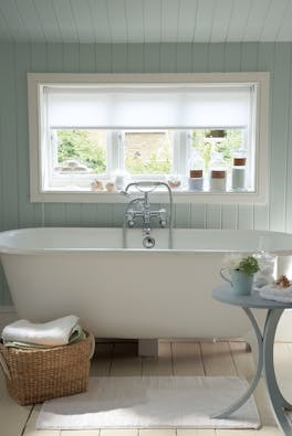 Paneled bathroom painted in light green (Salix) with a white bathtub under a large window.