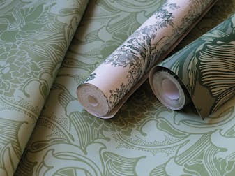 Two rolls of green wallpaper placed on top of a flat wallpaper roll.