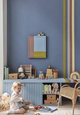 Child's playroom painted in dark blue (Juniper Ash) with multi colored stripes on the right, and toys placed on top of a unit with a child playing guitar.