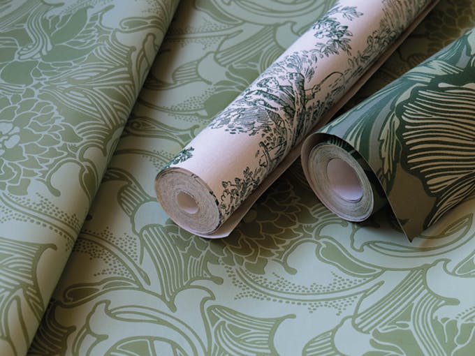 Two rolls of green wallpaper placed on top of a flat wallpaper roll.
