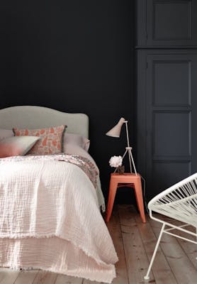 Bedroom painted in blue black 'Basalt' with a light pink bed and a contrasting bright orange stool.