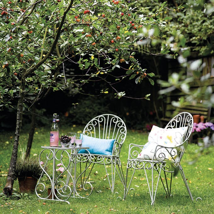 Two metal garden chairs painted in the grey-green shade 'Normandy Green', sitting on grass next to a small tree.