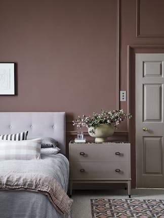 Bedroom painted in warm red (Nether Red) with contrasting grey woodwork and a bed scattered with cushions.