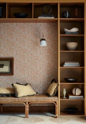 Reading nook featuring ditsy floral wallpaper (Spring Flowers - Bombolone) with shelving surround and a seat with scatter cushions.