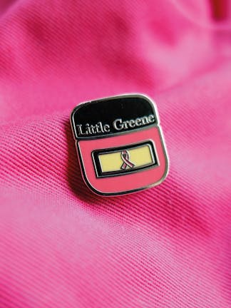 Little Greene and Breast Cancer Awareness Charity Pin Badge placed on bright pink fabric.