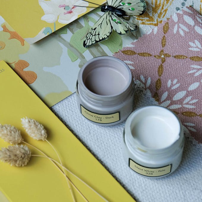 Two Little Greene paint sample pots open and placed on a moodboard with natural elements and wallpaper samples.