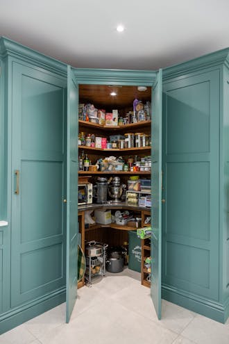 Blue-green kitchen cupboards with the middle ones open, revealing a pantry cupboard with food inside.