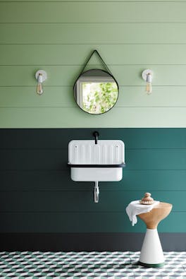 Paneled bathroom with the upper wall painted in Aquamarine and lower wall in dark green with a white sink and round mirror.