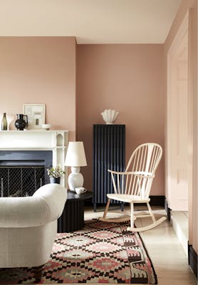 Pale pink living room in varying shades of Masquerade, alongside a rocking chair, sofa and Aztec rug. 