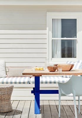 Outdoor dining area with off white paneled wall (Linen Wash) with a striped cushioned chair and wooden table.