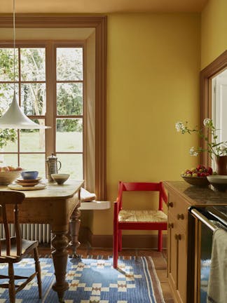 Kitchen painted in rich yellow shade 'Yellow-Pink' with deep gold 'Affogato' on the window frame, mid gold 'Middle Buff' on the ceiling and a bright red chair.