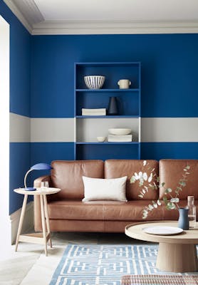 Living space with rich blue (Mazarine) wall and a contrasting neutral (Cool Arbour) stripe with a tan leather sofa.