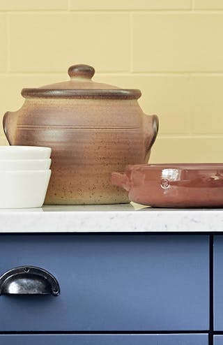 Close-up of a kitchen with yellow brick wall, blue cupboards and brown pots on the counter.