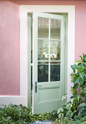 Exterior door painted in light green (Salix) with contrasting pale pink (Hellebore) wall surrounded by plants.