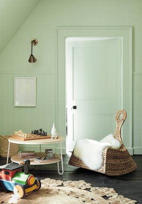 Children's nursery painted in pale green (Hidey Hole) with a rocking chair next to a round table and a chess board.