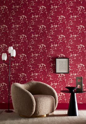 Living space featuring red scroll wallpaper (Tulip - Theatre), a fluffy gray armchair, a side table, lamp and framed picture.