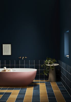 Deep blue (Royal Navy) bathroom with contrasting yellow and blue tiles and a large pink bathtub.