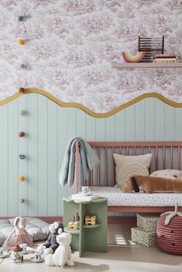 Child's playroom with ‘Lovers' Toile – Blush’ on the upper wall and ‘Aquamarine – Mid’ on the lower wall with a pink bench and toys on the floor.