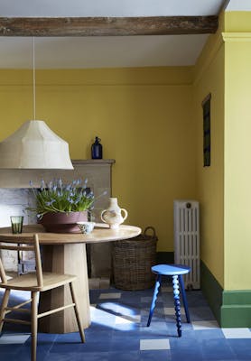 Dining room with vibrant yellow walls (Indian Yellow) with a green baseboard and wooden table and chairs. 