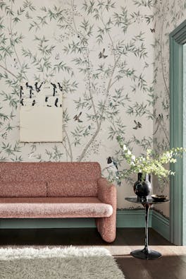 Living room with an off-white bird print mural wallpaper (Belton Scenic - Oyster) with a pink sofa and small table.