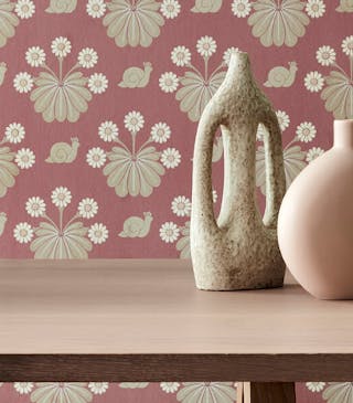 Close-up of pink printed snail wallpaper (Burges Snail - Rosie) behind a wooden dining room table.