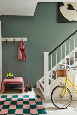 Grey green (Livid) painted hallway with grey carpeted stairs leading to a checkered rug and yellow bicycle. 