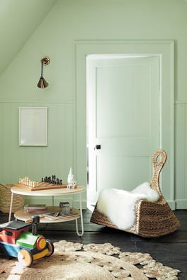 Children's nursery painted in pale green (Hidey Hole) with a rocking chair next to a round table and a chess board.