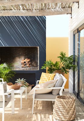 Outside seating area with blue-black (Basalt) and mustard yellow (Bassoon) walls, cushions, plants and a wicker basket.