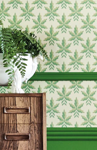 Close-up of leaf wallpaper (Clutterbuck - Lodge) alongside green panelling and a wooden chest of drawers.