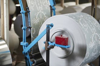 A large roll of grey and white Little Greene wallpaper in a factory.