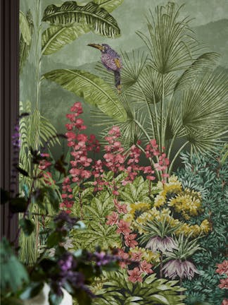 Close up of the vibrant green tropical mural wallpaper 'Capricorn - Boringdon' on a wall with a leafy plant in the foreground.