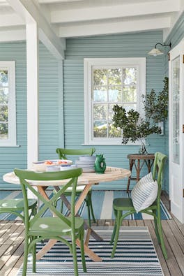 Outside dining area with cladded wall painted in pale blue (Celestial Blue) and a dining room table with green chairs.