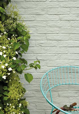 Exterior brick wall painted in grey green 'Normandy Grey' with a bush to the left and a Turquoise Blue chair to the right.