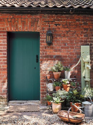 Brick exterior with a dark green (Goblin) door with several potted plants and a pebbled floor.