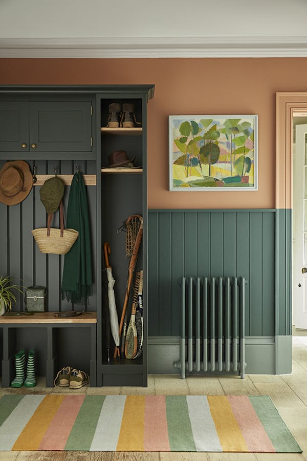 Paneled boot room with the top half painted in 'Split Pink' and the lower wall in 'Harley Green' with a cupboard to the left and a multi-colored stripy rug.